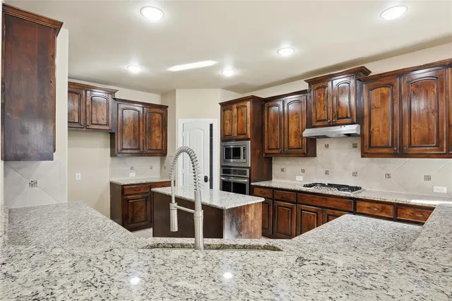a kitchen with stainless steel appliances kitchen island granite countertop a sink stove and refrigerator