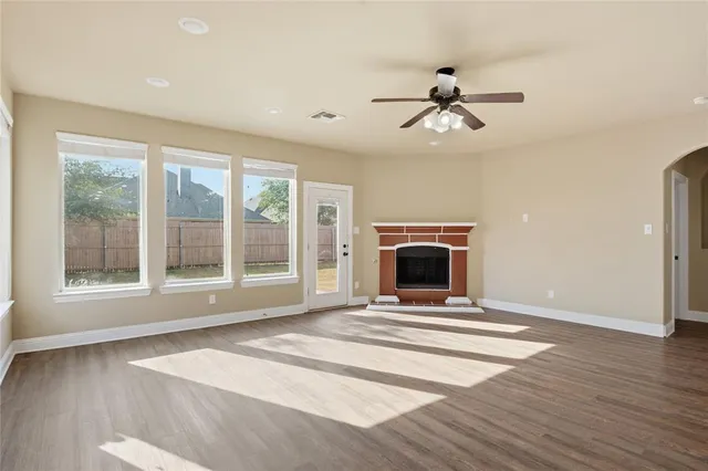 a view of an empty room with window a fireplace and a ceiling fan