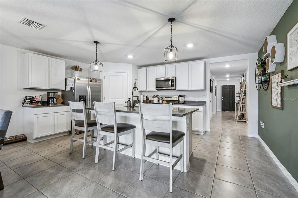 3139 Silver Date Drive Wimauma, FL 33598 - Photo 9 of 47 a kitchen with stainless steel appliances kitchen island granite countertop a refrigerator a stove a sink a dining table and chairs with wooden floor