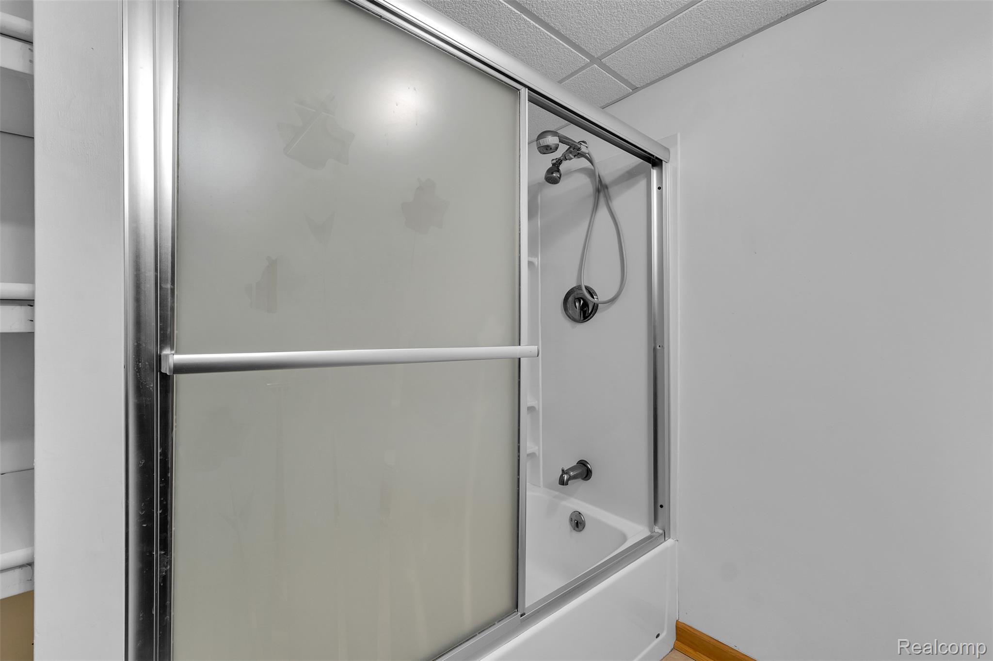 7000 Woonsocket Street Canton, MI 48187 - Photo 56 of 65 Bathtub with a sliding frosted glass shower enclosure and a chrome showerhead