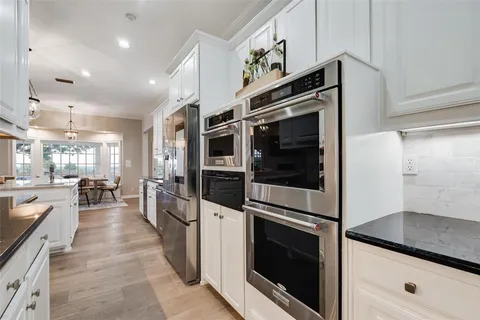 a large kitchen with stainless steel appliances kitchen island granite countertop a stove a sink a refrigerator and a dining table with wooden floor