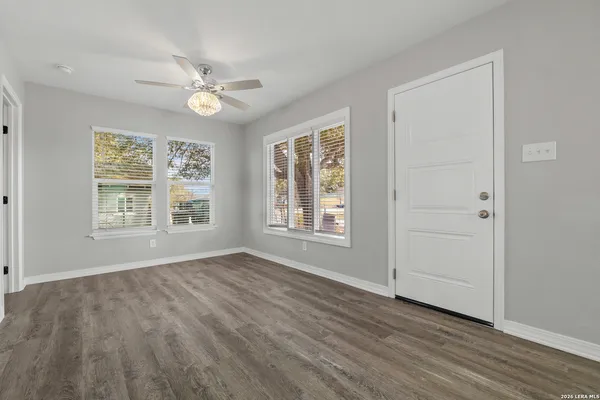 an empty room with wooden floor chandelier fan and windows