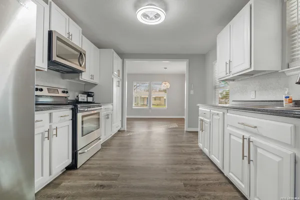 a kitchen with stainless steel appliances granite countertop a stove top oven a sink dishwasher and white cabinets with wooden floor