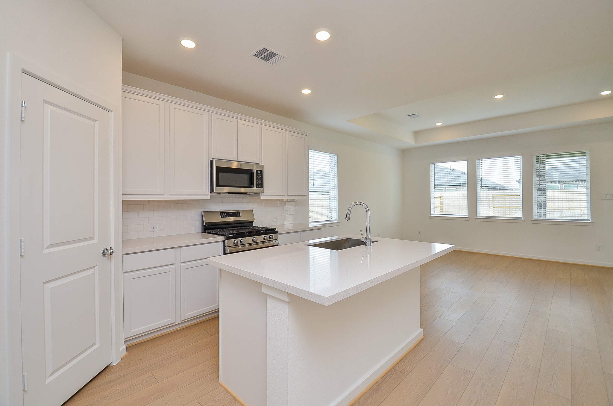 9727 Rialto Hts Drive Cypress, TX 77433 - Photo 12 of 37 This photo shows a bright, open-concept space featuring a modern kitchen with white cabinets and stainless steel appliances. It flows into a spacious living area with light color flooring and ample natural light from large windows.