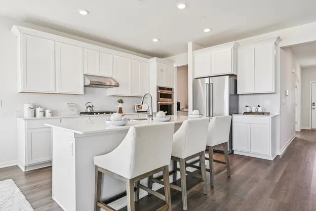 a kitchen with stainless steel appliances a white refrigerator a sink a stove a dining table and chairs