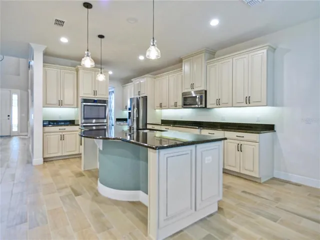 a kitchen with kitchen island granite countertop a stove a sink a refrigerator and white cabinets with wooden floor