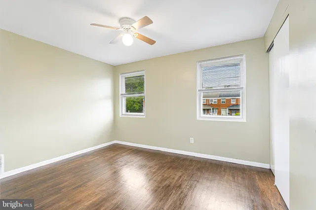 an empty room with wooden floor chandelier fan and windows