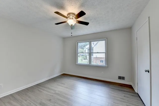 an empty room with wooden floor chandelier fan and windows