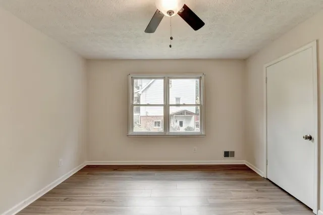 an empty room with wooden floor chandelier fan and windows