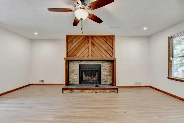 an empty room with windows fireplace and wooden floor