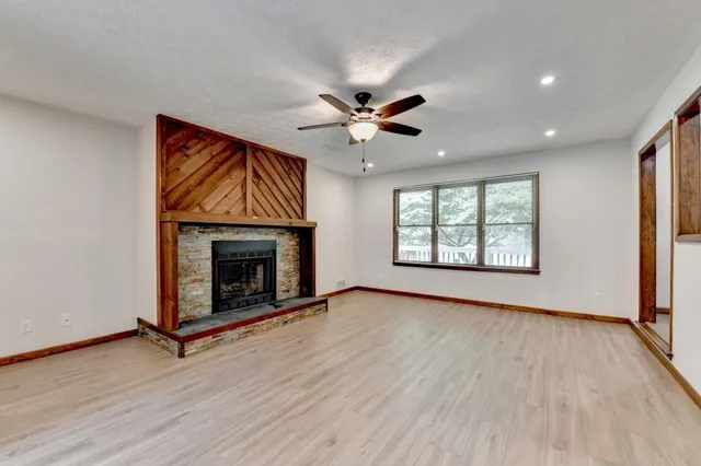an empty room with windows a fireplace a ceiling fan and wooden floor