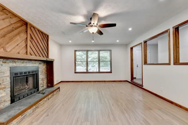 an empty room with windows fireplace and fan
