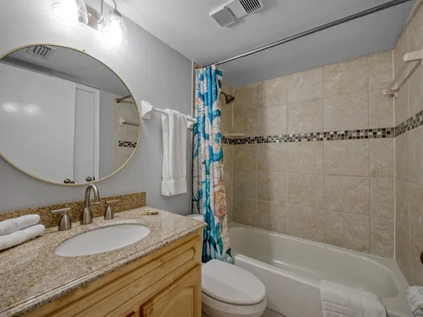 a bathroom with a granite countertop bathtub shower sink vanity mirror and toilet