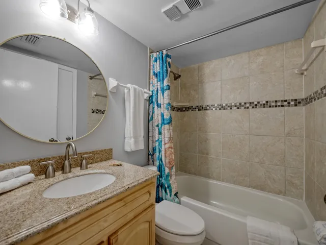 a bathroom with a granite countertop bathtub shower sink vanity mirror and toilet