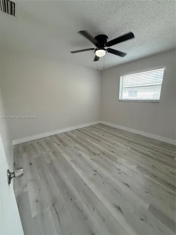 an empty room with wooden floor fan and windows