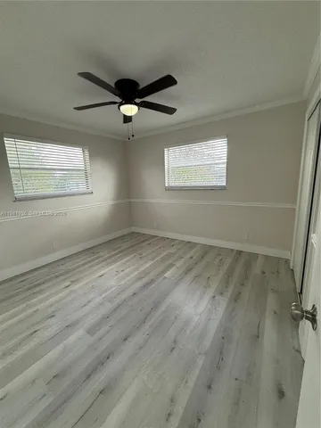 an empty room with wooden floor fan and windows