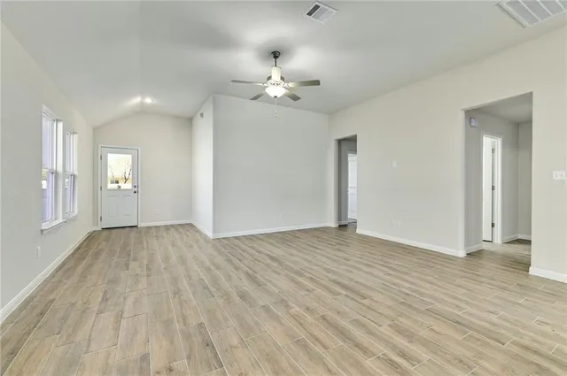 an empty room with wooden floor fan and windows