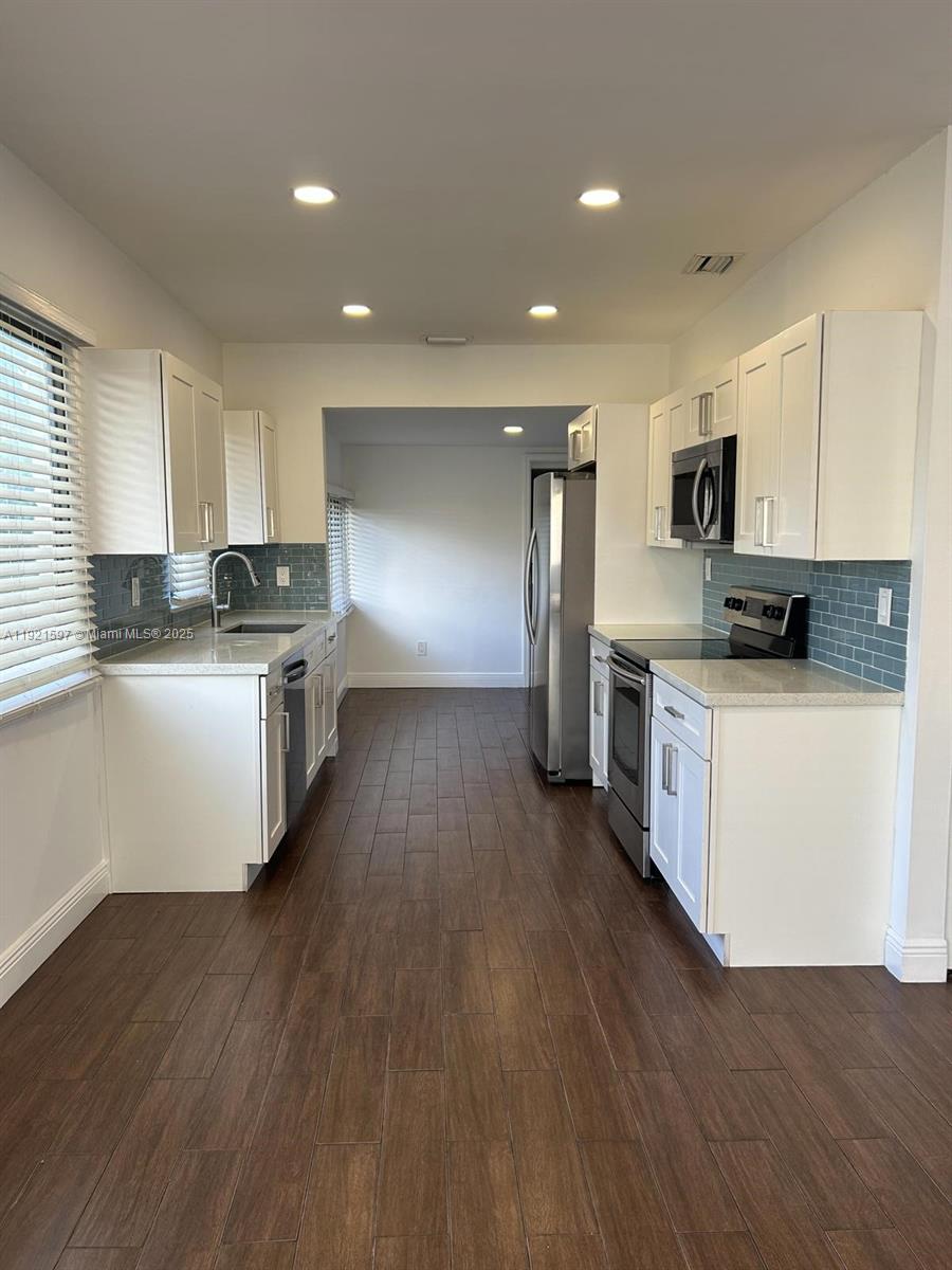 5790 Southwest 5th Street Miami, FL 33144 - Photo 6 of 31 a kitchen with stainless steel appliances a microwave a stove a sink dishwasher a refrigerator and white cabinets with wooden floor