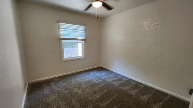an empty room with a chandelier fan and windows