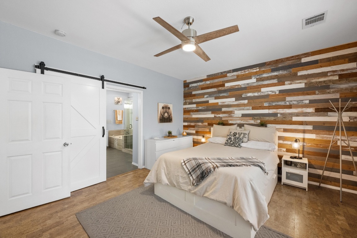 12201 Barrel Bend Austin, TX 78748 - Photo 17 of 35 Bedroom with wood walls, light wood finished floors, a ceiling fan, a barn door, and ensuite bathroom