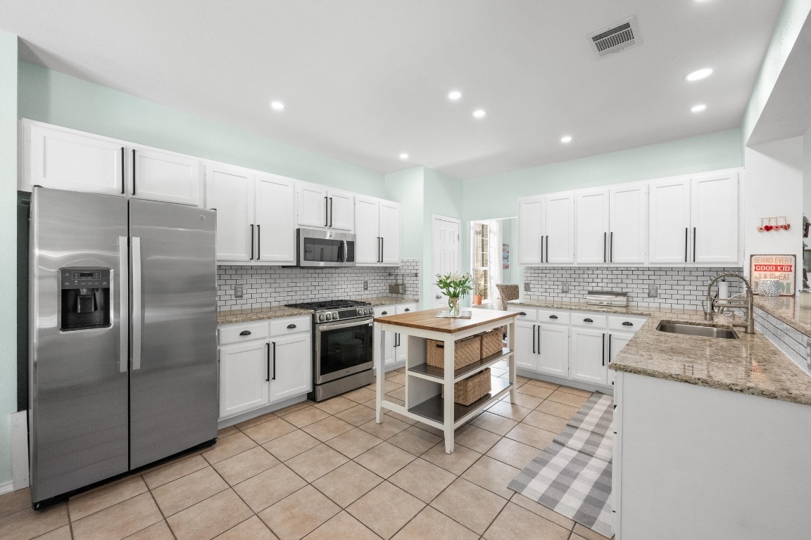 12201 Barrel Bend Austin, TX 78748 - Photo 8 of 35 Kitchen with light stone countertops, appliances with stainless steel finishes, white cabinetry, open shelves, and light tile patterned floors