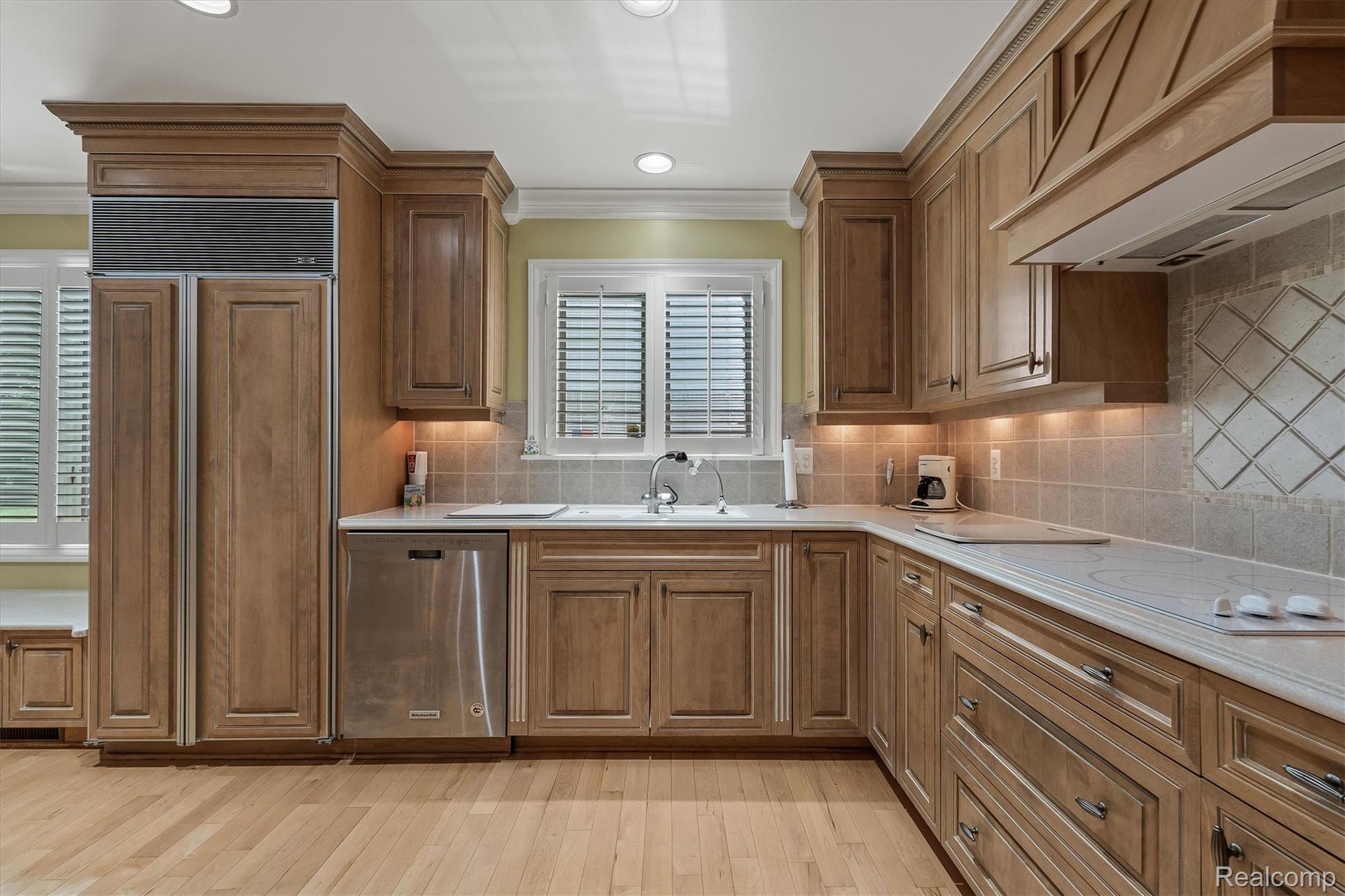 1662 Sumac Drive Rochester, MI 48309 - Photo 13 of 38 Kitchen featuring wood cabinetry with crown molding, stainless steel dishwasher, light-toned countertops, and a tiled backsplash with decorative inlay