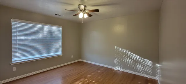 a view of empty room with wooden floor and fan