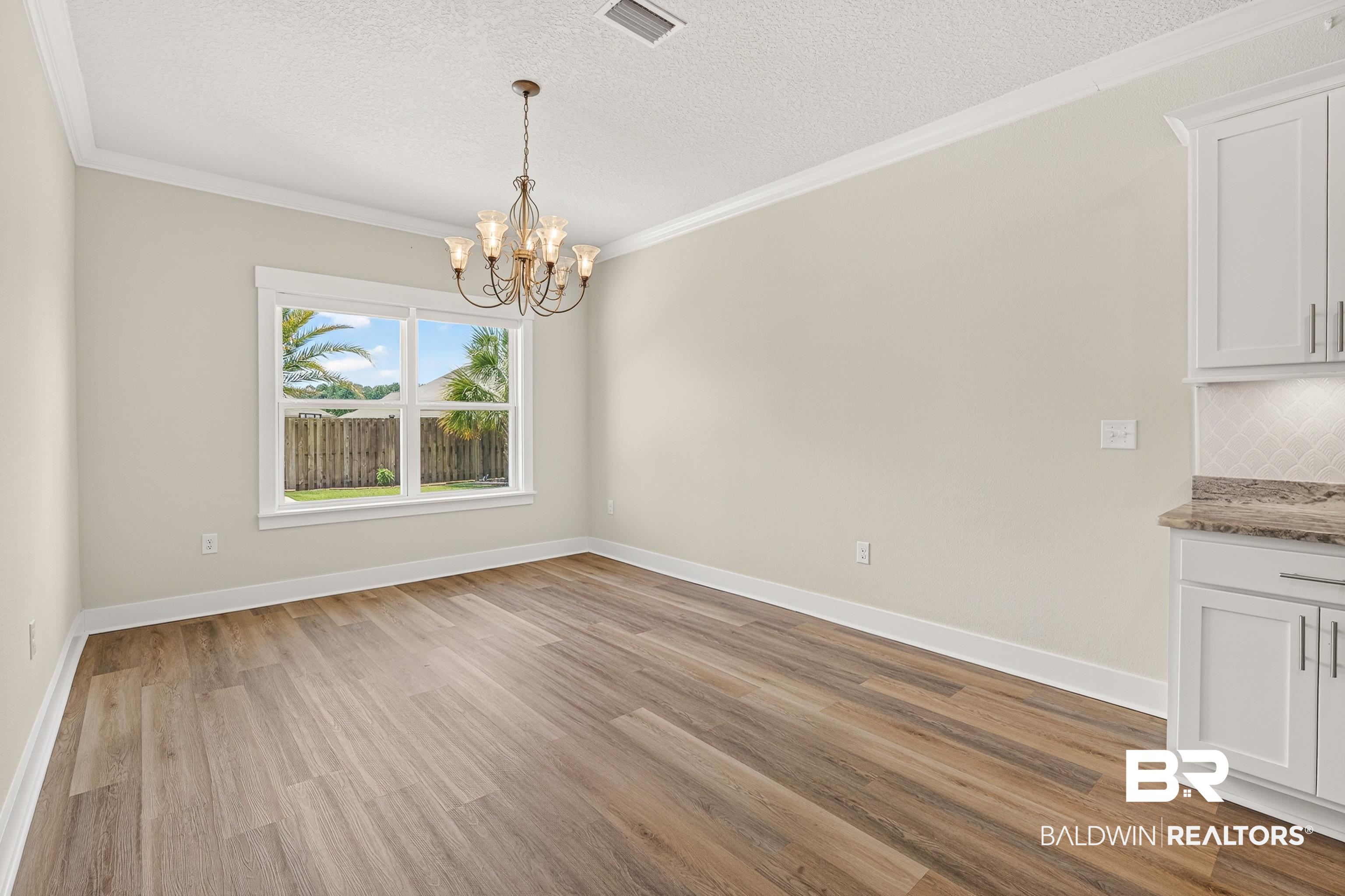 1724 Partridge Street Foley, AL 36535 - Photo 22 of 62 Spacious room featuring wood-finish flooring, a large window with white trim, a decorative chandelier, and crown molding