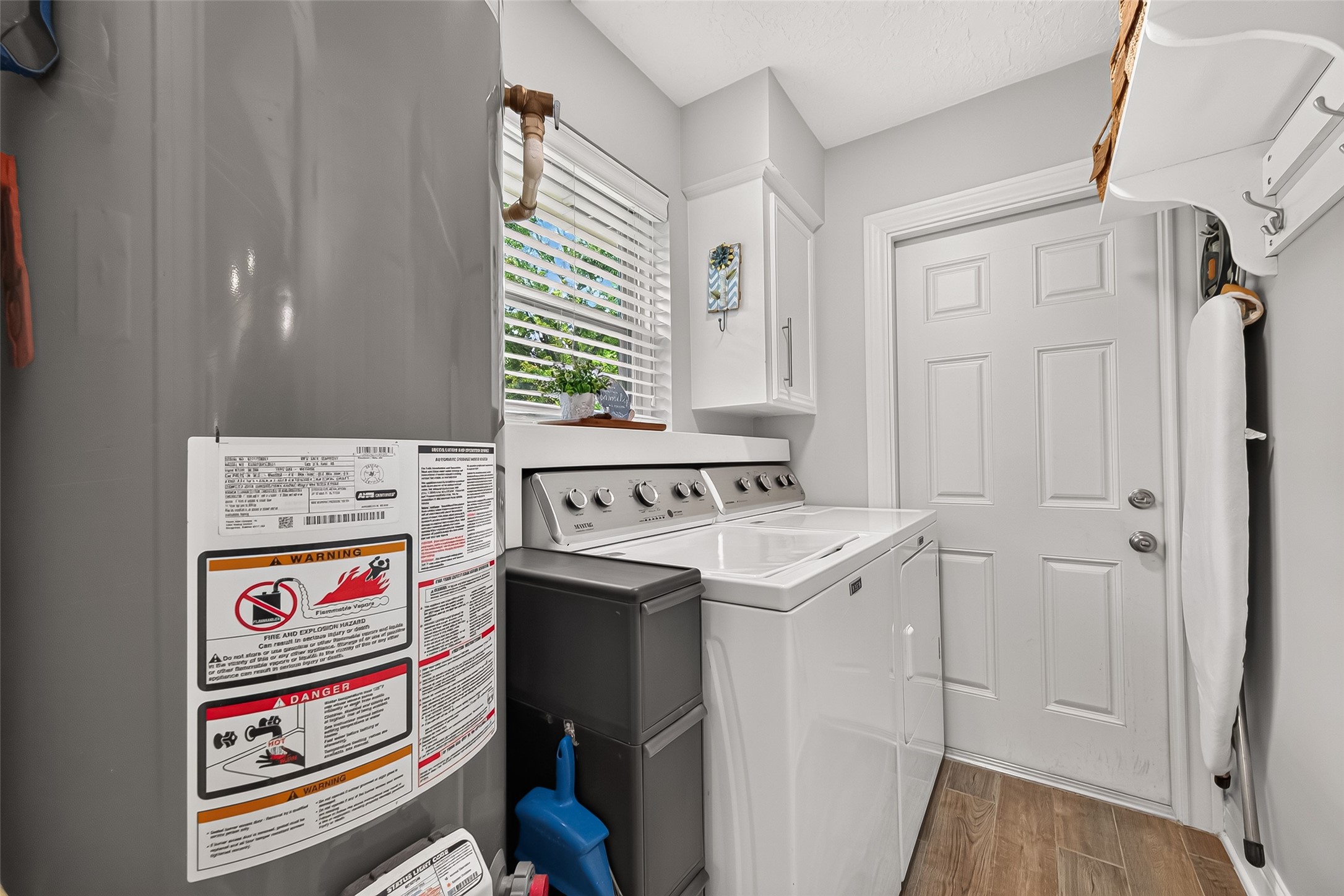 24719 Wilderness Road Spring, TX 77380 - Photo 18 of 42 This photo shows a laundry room adjacent to a water heater. There's a window with blinds, a door, and some storage space including a small cabinet and shelf. The room has ceramic tile flooring and light gray walls. Accessible from garage and kitchen.