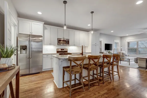 a kitchen with stainless steel appliances kitchen island granite countertop a refrigerator a stove a sink a microwave and a dining table with wooden floor