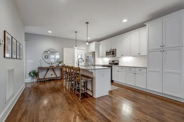 a kitchen with stainless steel appliances granite countertop a refrigerator a microwave oven a sink dishwasher and white cabinets with wooden floor