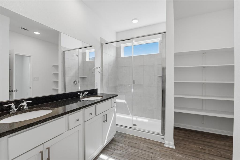 201 Betsy Road Hutto, TX 78634 - Photo 13 of 18 Bathroom featuring a double vanity with dark countertops, a spacious glass-enclosed shower with a window, and built-in shelving for storage