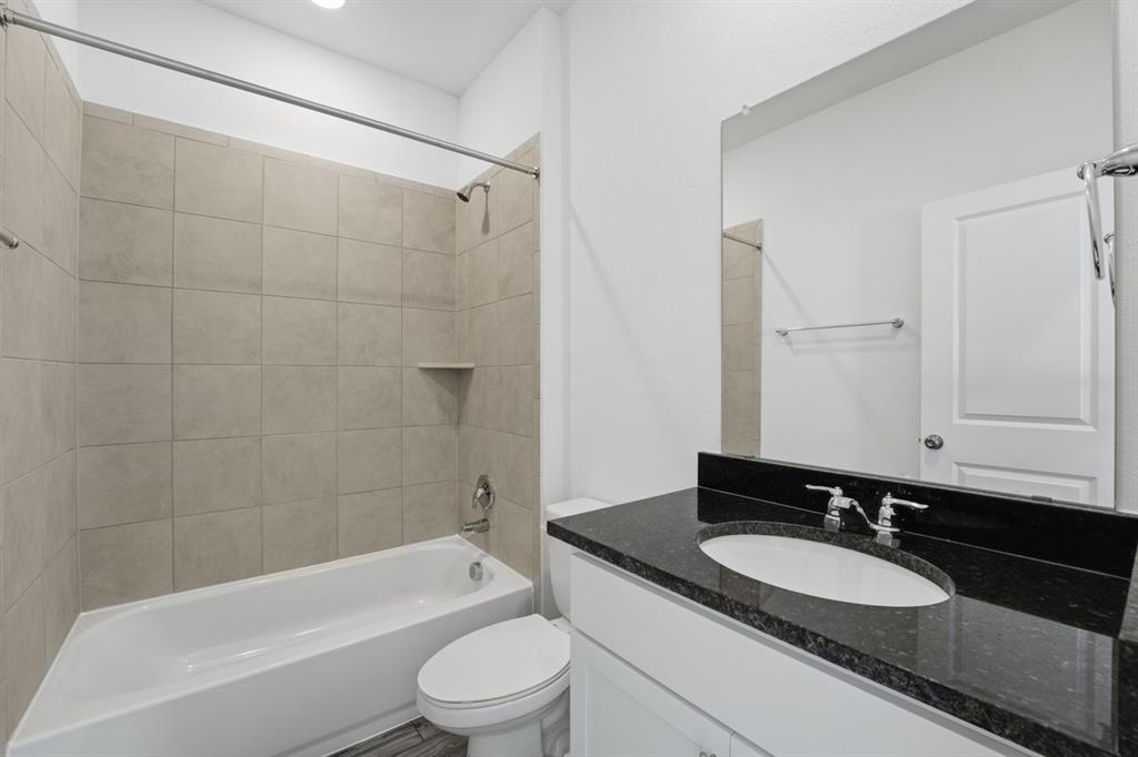 201 Betsy Road Hutto, TX 78634 - Photo 14 of 18 Bathroom featuring a white vanity with a black countertop, a wall-mounted mirror, and a shower-tub combination with light-colored tile surround