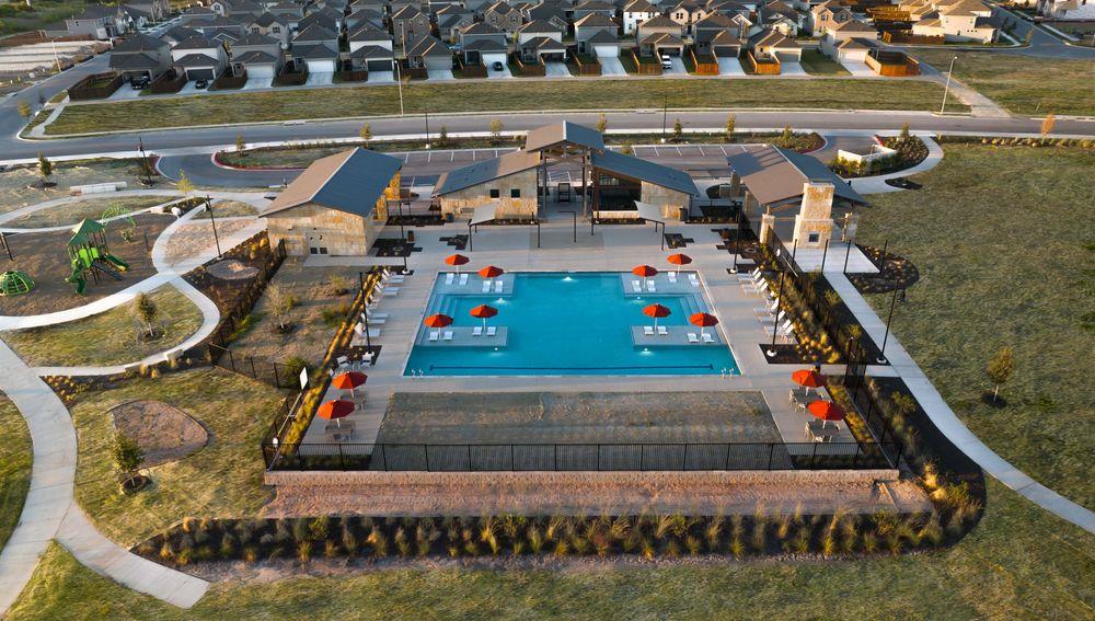 201 Betsy Road Hutto, TX 78634 - Photo 6 of 18 Community amenities featuring a swimming pool with lounge chairs and red umbrellas, a playground, and paved pathways, surrounded by landscaped green spaces