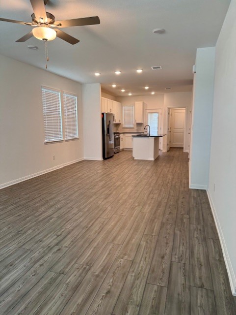 201 Betsy Road Hutto, TX 78634 - Photo 9 of 18 The property features an open living area with wood-look flooring and a ceiling fan, leading into a kitchen equipped with stainless steel appliances, white cabinetry, and recessed lighting