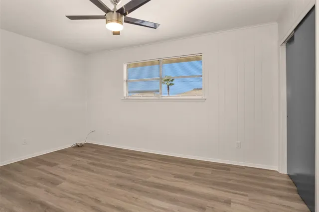 a view of an empty room with wooden floor and a ceiling fan
