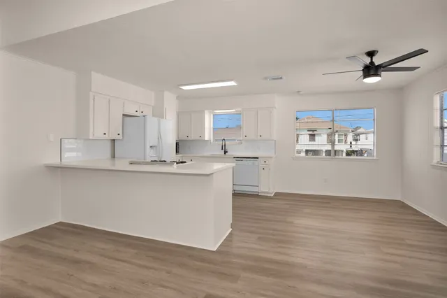 a large white kitchen with kitchen island a sink dishwasher a stove and a refrigerator with wooden floors
