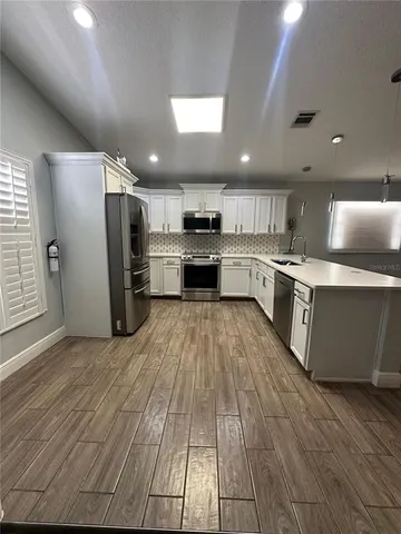 a large kitchen with stainless steel appliances kitchen island a large counter top and wooden floors