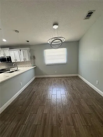 an empty room with wooden floor kitchen view and windows