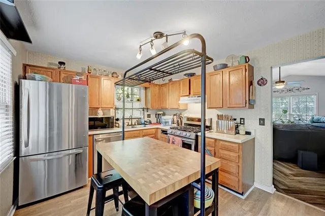 a kitchen with granite countertop a refrigerator a stove a sink dishwasher and wooden cabinets with wooden floor