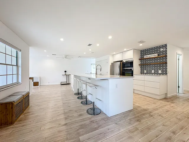 a large white kitchen with wooden floor and stainless steel appliances