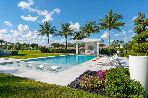 a view of swimming pool with lawn chairs and large trees