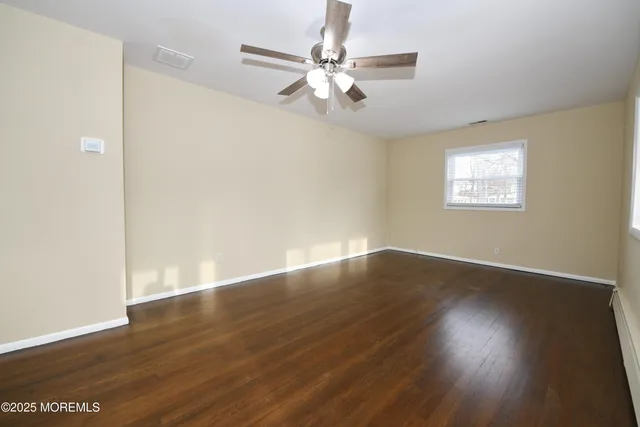 a view of an empty room with wooden floor and a ceiling fan