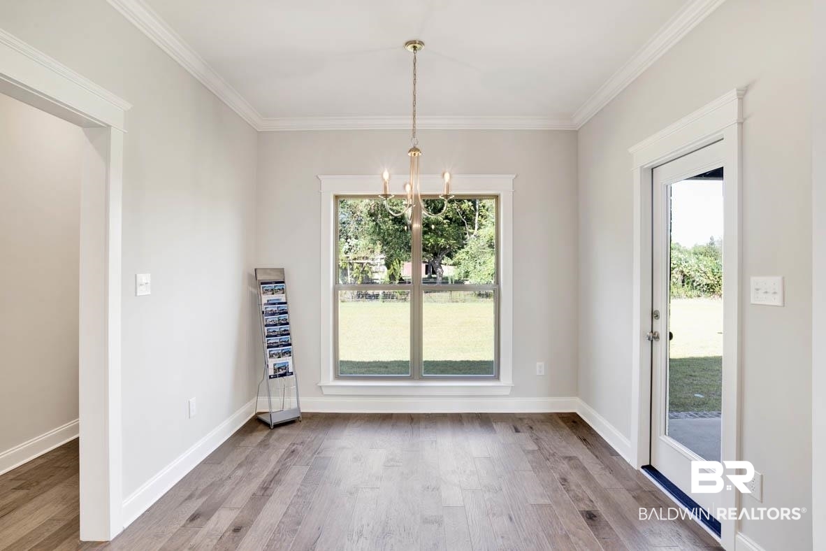 393 Garrison Boulevard Fairhope, AL 36532 - Photo 17 of 40 Unfurnished dining area with light hardwood / wood-style flooring, ornamental molding, a notable chandelier, and a healthy amount of sunlight