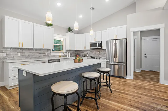 a kitchen with stainless steel appliances a sink a stove a refrigerator and white cabinets with wooden floor