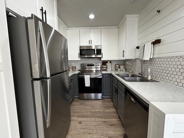 608 South 500 West, Unit 3 Provo, UT 84601 - Photo 10 of 35 Galley kitchen featuring stainless steel appliances, two-tone cabinetry with black hardware, hexagon tile backsplash, light wood-finish flooring, and light-toned countertops