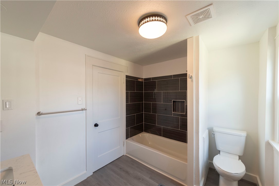 1022 North Howard Street Akron, OH 44310 - Photo 14 of 38 Far shot of second floor bath showing bathtub with tile surround, commode, and luxury vinyl tile flooring.