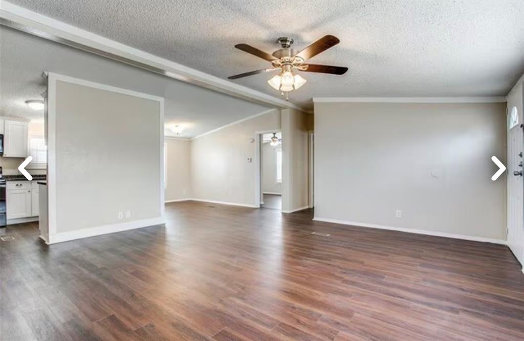 168 Prairie Lane Azle, TX 76020 - Photo 3 of 16 Unfurnished living room featuring dark wood-type flooring, a ceiling fan, a textured ceiling, ornamental molding, and vaulted ceiling