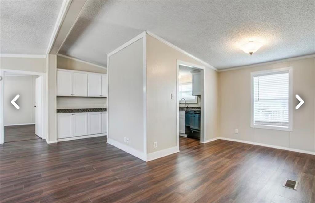 168 Prairie Lane Azle, TX 76020 - Photo 6 of 16 Unfurnished living room with a textured ceiling, dark wood-style floors, ornamental molding, vaulted ceiling, and plenty of natural light