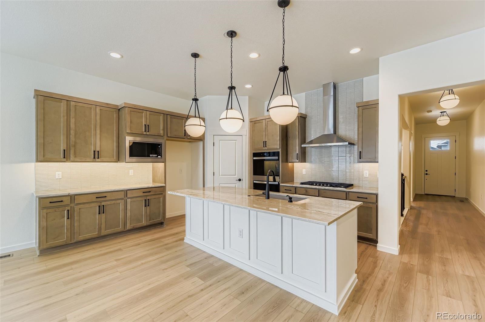 8942 South Riviera Way Aurora, CO 80016 - Photo 9 of 29 a large kitchen with granite countertop a stove a sink a center island a refrigerator and a wooden floor